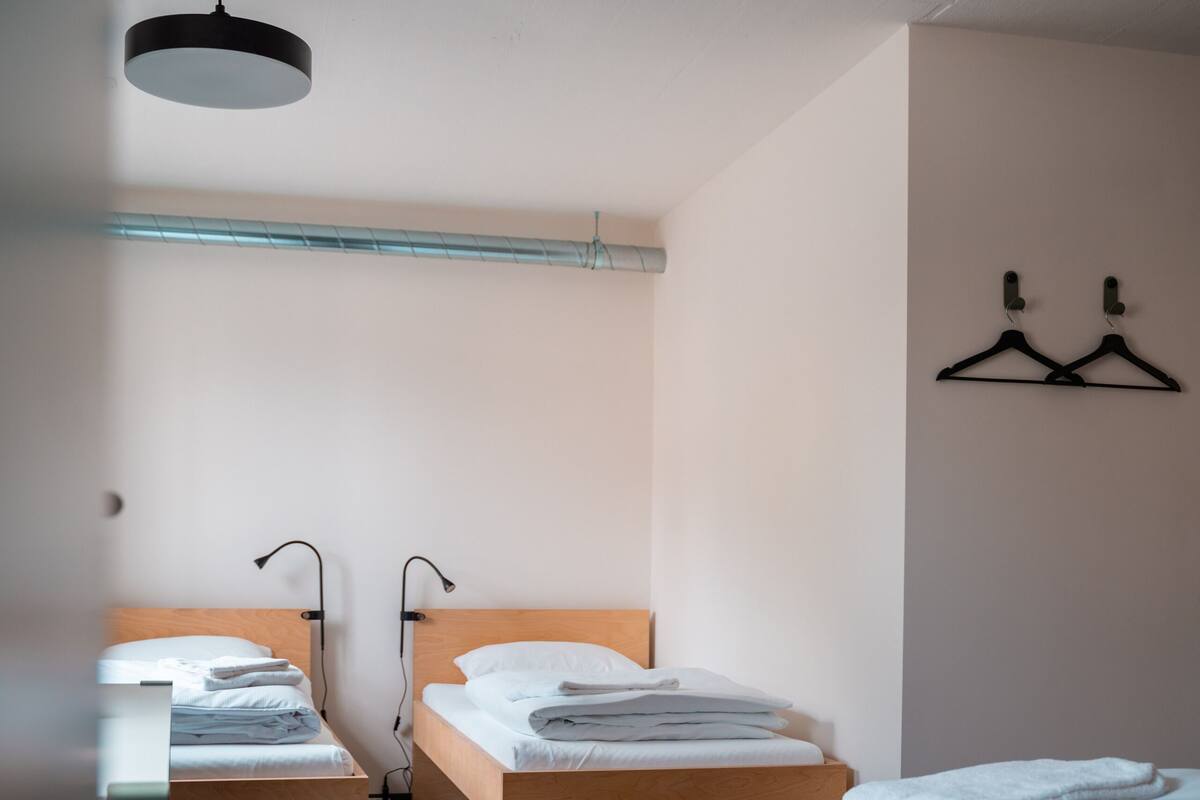A hotel room with two single beds, a wooden headboard, a hanging light fixture, and a wall-mounted coat rack.