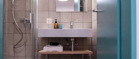 Un baño moderno con cabina de ducha de vidrio, un lavamanos blanco con espejo y un estante de madera.