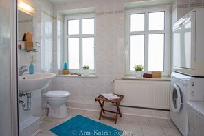Enjoy a clean and minimalist bathroom with a sink, toilet, and compact washing machine, plus a comfortable stool and rug.