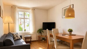 En moderne stue med sofa, spisebord, stole, et fjernsyn og et vindue med gardiner.