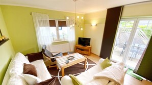 A living room with a sofa, armchairs, a coffee table, a TV, and a window with curtains. - Ferienhaus "sabrina" (Sassnitz)
