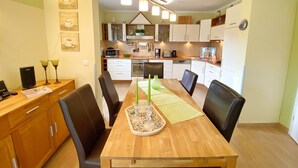 A dining area with a wooden table, chairs, and a kitchen in the background. - Ferienhaus "sabrina" (Sassnitz)