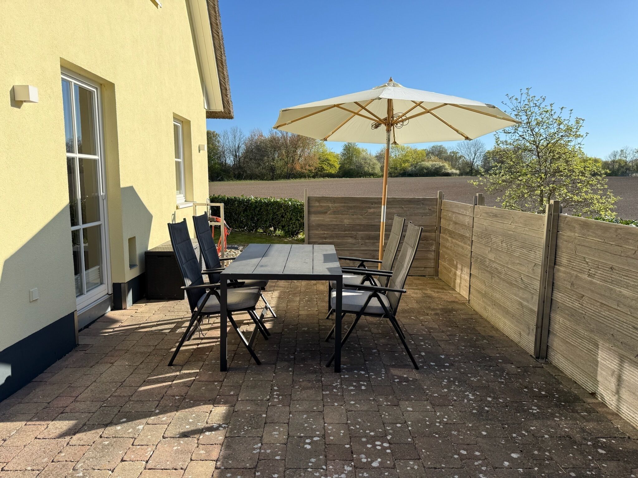Eine Terrasss mit Tisch und Stühlen, einem großen Sonnenschirm und einem Holzzaun.