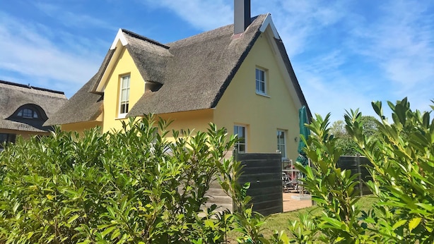 A yellow house with a thatched roof and a chimney, surrounded by greenery. - Ferienhaus "sarcander" (Glowe)