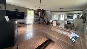 A spacious living area with a wooden coffee table, a leather sofa, a TV, and a staircase leading to an upper level. - Ferienhaus "sarcander" (Glowe)