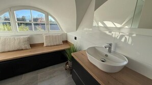 A modern bathroom with a skylight, a large mirror, and a wooden vanity. - Ferienhaus "sarcander" (Glowe)