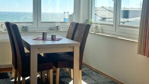 Zona de menjador amb taula i cadires, una finestra amb vista al mar i una làmpada decorativa.