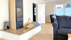 A modern living room with a built-in fireplace, a dark sofa, and a large window. - Reethaus Vilmnitz - Ferienwohnung "muglitz" (Vilmnitz)