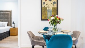 Una habitación de hotel moderna con una cama, una mesa de comedor con platos y vasos, y un jarrón de flores.