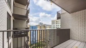 Un balcón con barandilla metálica, una mesa de vidrio y vistas de edificios circundantes.
