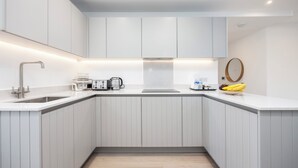 Una cocina moderna con armarios blancos, un lavamanos de acero inoxidable y una encimera con cafetera, tostadora y plátanos.