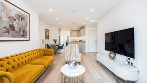 Una sala de estar moderna con un sofá color mostaza, un sillón a rayas, una mesa de centro blanca y un televisor montado en la pared.
