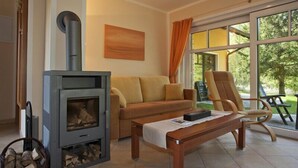 Ein Wohnzimmer mit Kaminofen, einer Couch, einem Couchtisch und Blick ins Freie durch große Fenster.