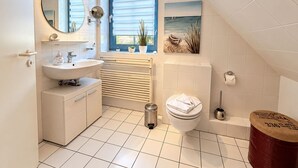 Un baño moderno con lavamanos, espejo, inodoro y ventana con persianas.