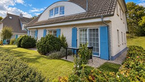 Una casa de dos pisos con techo curvo, contraventanas azules y un jardín bien cuidado.