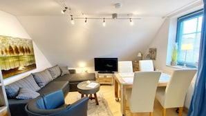 Una sala de estar moderna con un sofá, una mesa de centro, un televisor y un comedor con sillas y una mesa.