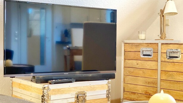 Un televisor de pantalla plana sobre un baúl de madera, una lámpara y una vela en una mesa.