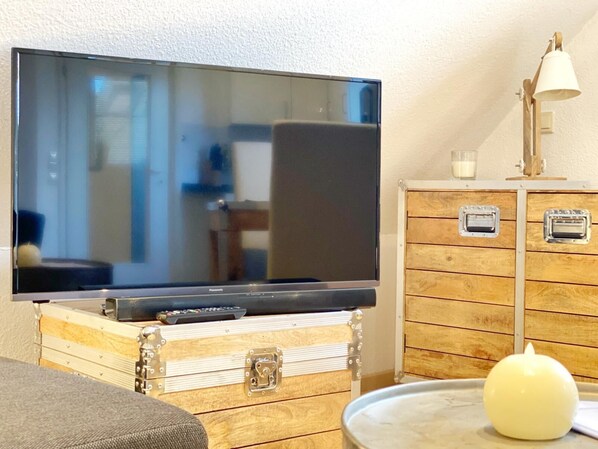 A flat-screen TV on a wooden chest, a lamp, and a candle on a table. - Wohnung 24 "lakeview" Am Neuensiener See (Sellin OT Seedorf)