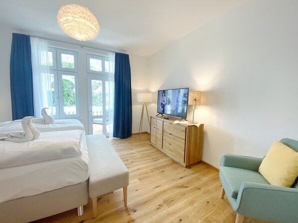 Ein Hotelzimmer mit Bett, Fernseher, einem Holzschrank, einer Couch und einem großen Fenster mit Vorhängen.