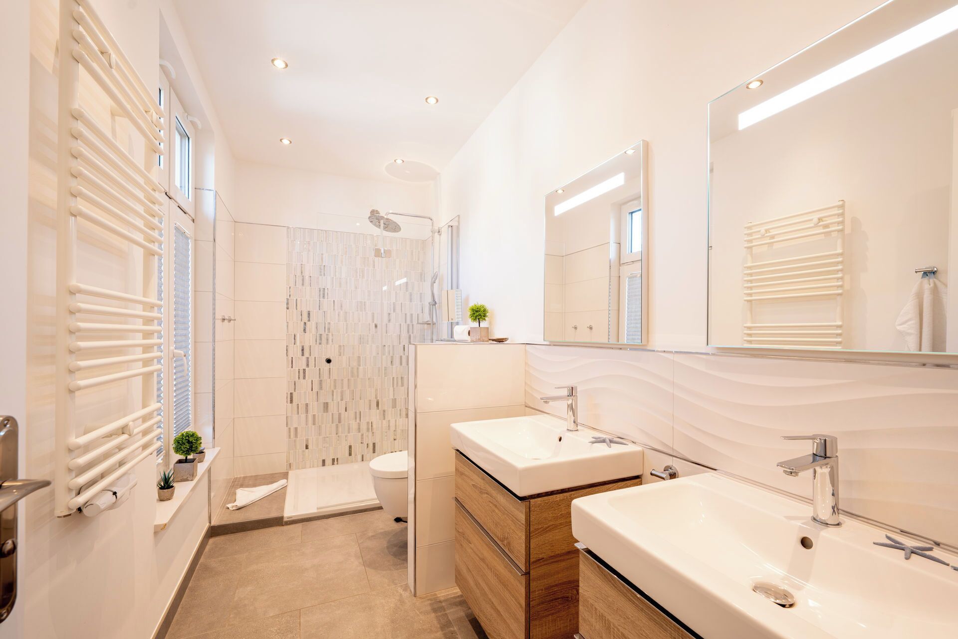 Ein modernes Badezimmer mit Dusche, zwei Waschbecken, einem großen Spiegel und einem Handtuchhalter.