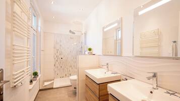 Ein modernes Badezimmer mit Dusche, zwei Waschbecken, einem großen Spiegel und einem Handtuchhalter.