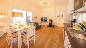 A modern kitchen with a built-in oven, a dining area with a table set for four, and a living room with a sofa and TV.