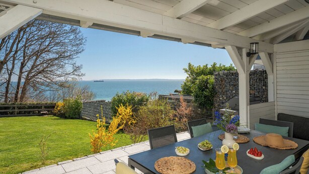 An outdoor patio with a table set for dining, overlooking a body of water and a distant ship.