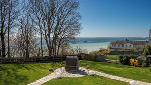 A coastal property with a stone pathway leading to a seating area, a view of the sea, and a house with a stone wall.