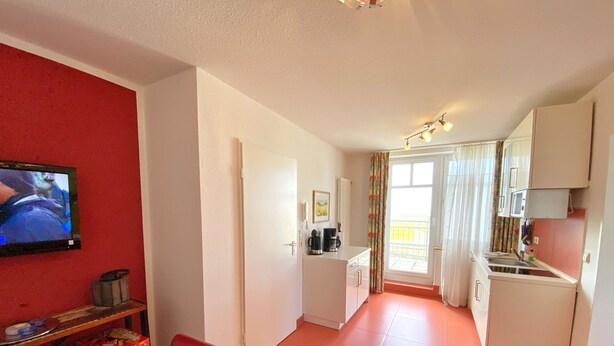 Ein kompakter Wohnbereich mit Küchenzeile, Essplatz und Fernseher an der Wand.