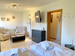 A hotel room with two beds, a sofa, a cabinet, a TV, and artwork on the walls.
