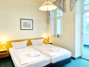 A hotel room with two beds, a framed picture on the wall, a window with curtains, and a door leading outside.