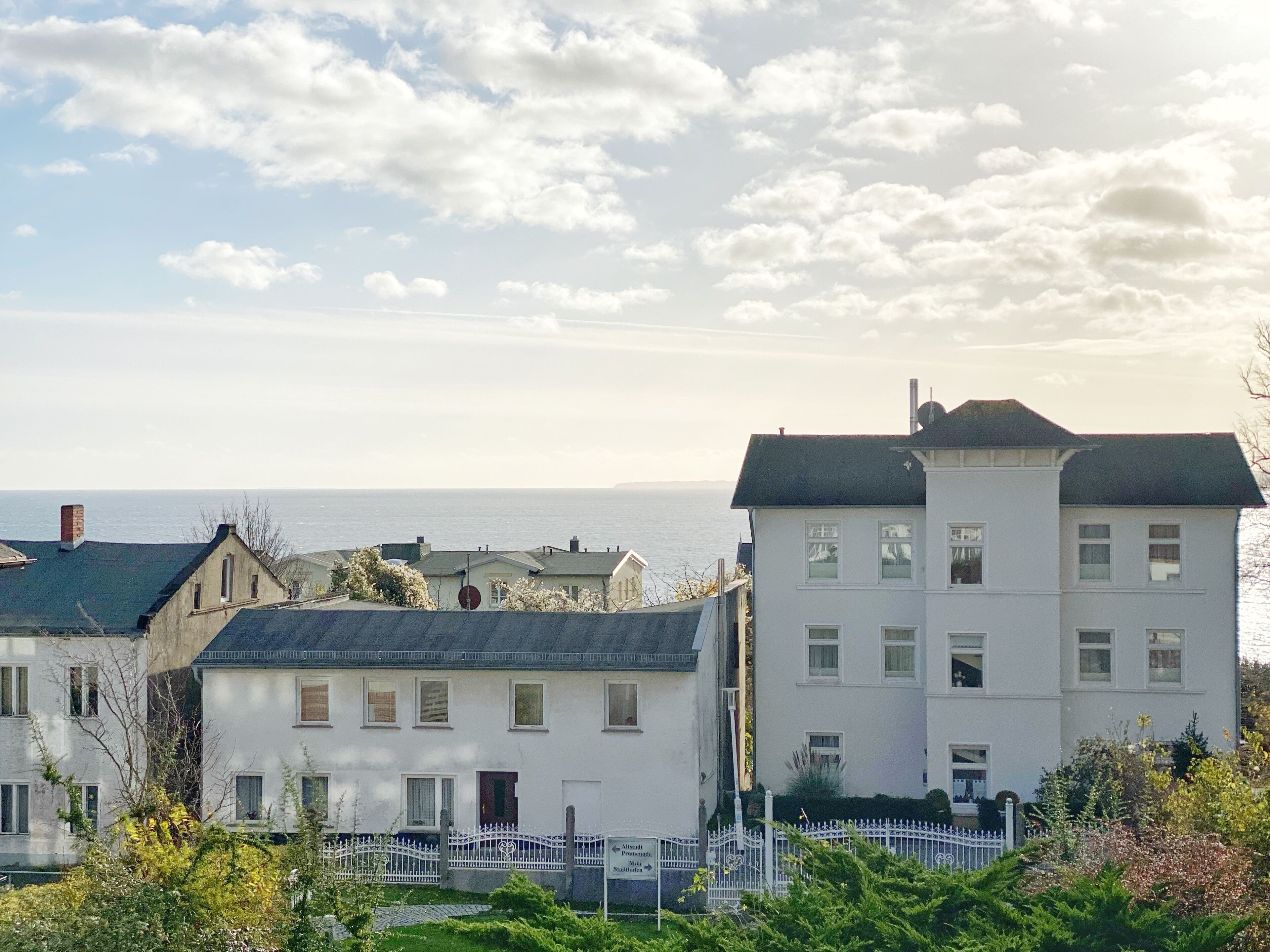 Un quartier résidentiel situé sur la côte, avec des maisons, une clôture blanche et une vue dégagée sur la mer.