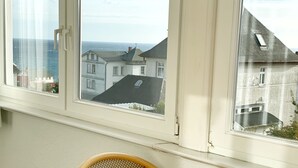 Ein Zimmer mit Tisch und Stühlen, ein Fenster mit Blick auf Gebäude und das Meer.
