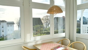 Ein Essbereich mit Tisch und Stühlen, einer Korblampe und Blick auf Gebäude und Bäume.