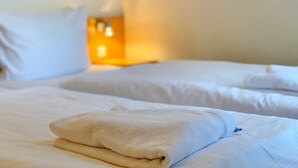 Ein ordentlich gemachtes Bett mit zusammengelegtem Handtuch und einem Nachttisch mit Lampe.