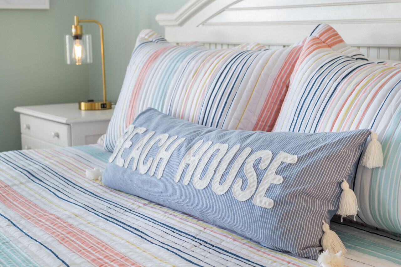 Ein Bett mit gestreifter Bettwäsche und einem Kopfkissen mit dem Aufdruck "Beach House".