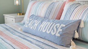 Una cama con ropa de cama a rayas y una almohada con la inscripción "Beach House".