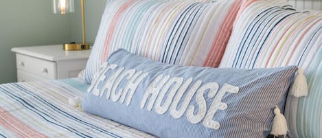 Una cama con ropa de cama a rayas y una almohada con la inscripción "Beach House".