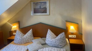 A hotel room with a sloped ceiling, a bed with patterned bedding, two bedside lamps, and a framed picture on the wall.