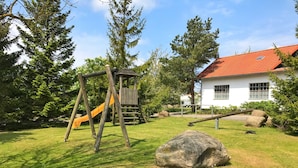 A playground with a slide and swings, a large rock, and a house with a red roof. - Landpension Dubnitz - Holiday apartment 2 (Sassnitz)