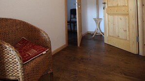 Une pièce avec un fauteuil en osier, une porte en bois et un porte-manteau.