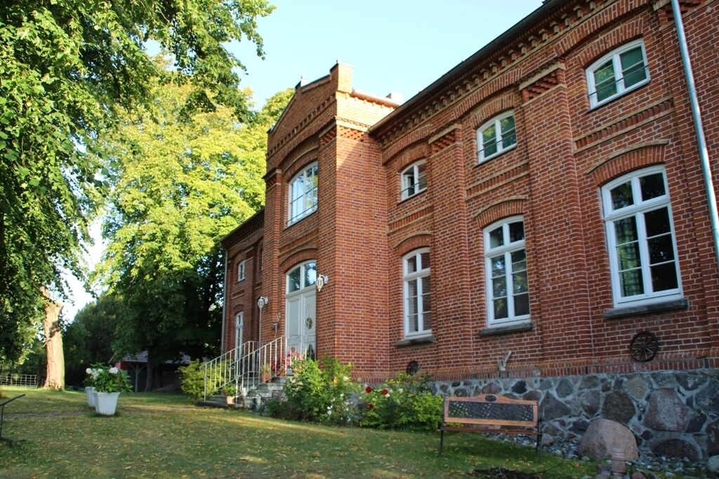 Ein rot genauberes Gebäude mit Steinfundament, großen Fenstern und einer kleinen Veranda mit Stufen.