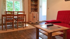 Un saló amb una taula de dinar de fusta, cadires, un sofà vermell, una taula de centre de vidre i un armari de fusta amb prestatges.