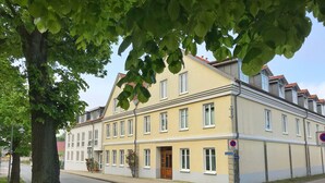 En bygning med flere etager, en gul facade, hvide vinduesrammer og et rødt tegltag.