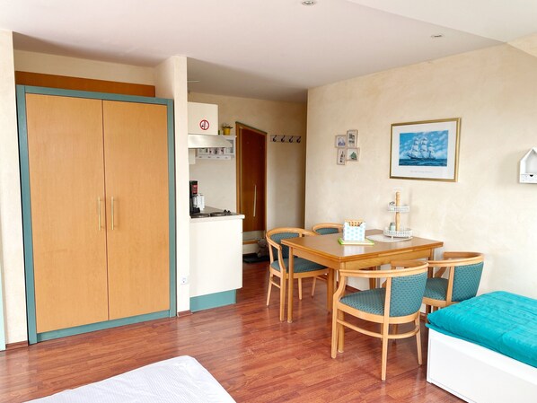 Une pièce de taille modeste comprenant une armoire en bois, un coin cuisine, une table à manger avec des chaises et un lit.