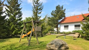A playground with a slide and swings, a large rock, and a house with a red roof.
