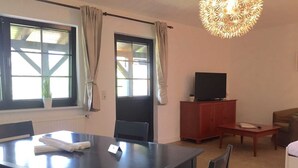 A room with a dining table, chairs, a television on a cabinet, a sofa, and a decorative light fixture.