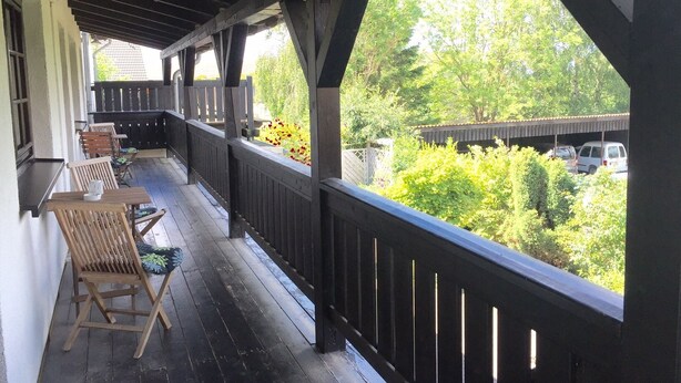A covered porch with wooden chairs and a view of a parking area and greenery.