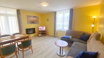 A living room with a sofa, a TV, a dining table with chairs, and a small round table.