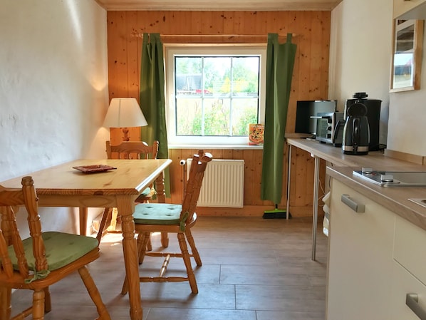 A cozy kitchen with wooden walls, a dining table with chairs, a window with curtains, and a coffee maker on the counter.